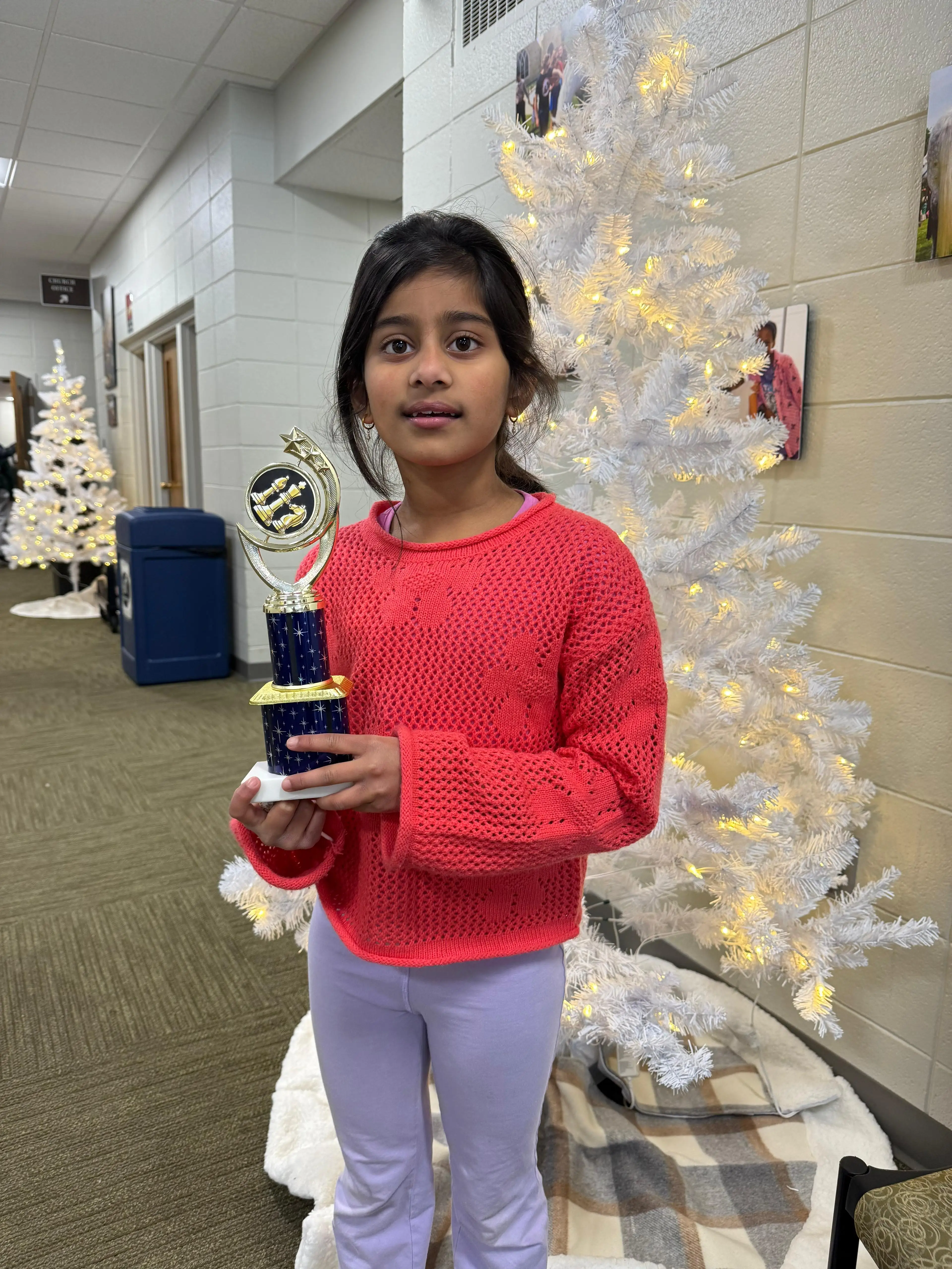 A young boy proudly holding a golden knight chess piece trophy, standing beside his Chess instructor
